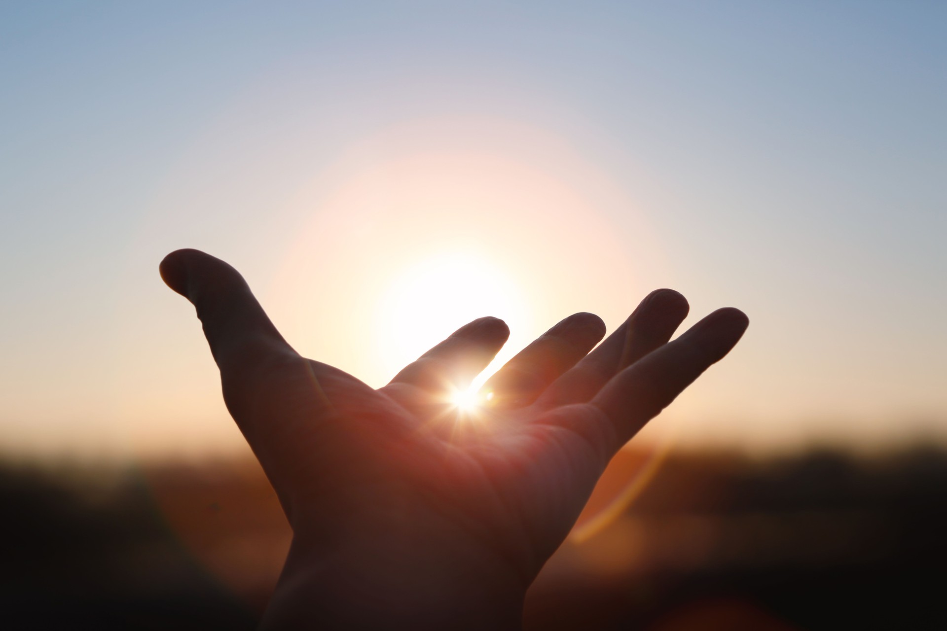 Hands stretched out toward the rising sun at New Year's sunrise, brilliant light shining between fingers, future hope and hope concept
